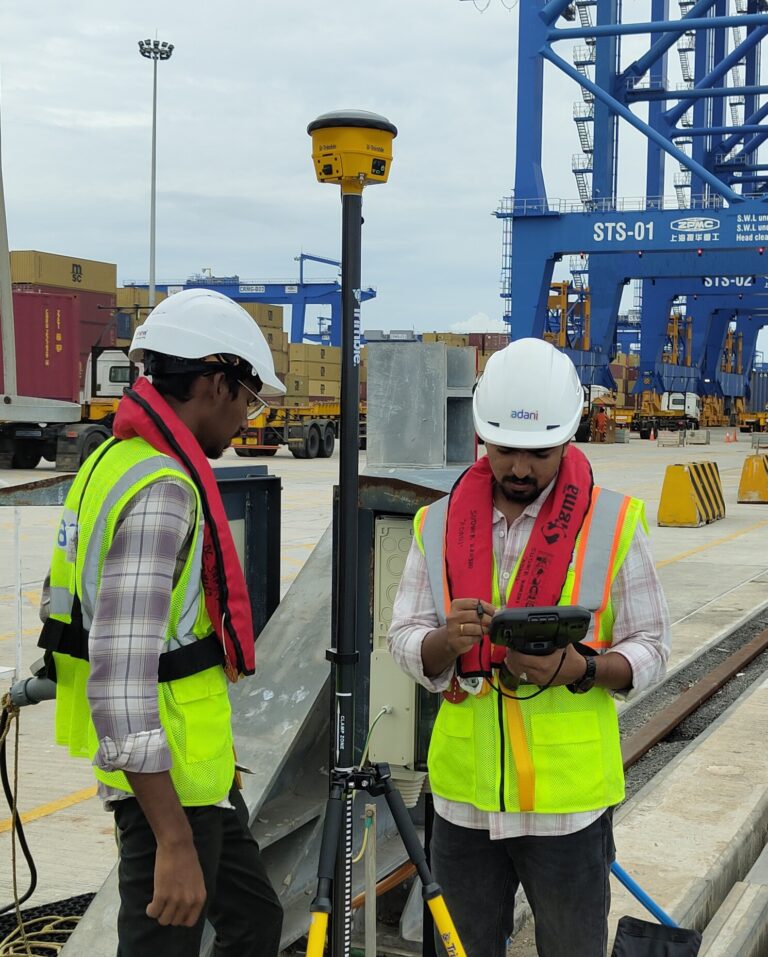 Survey engineers using a Trimble GNSS receiver for RTK positioning and geospatial data collection at a port and container terminal facility.